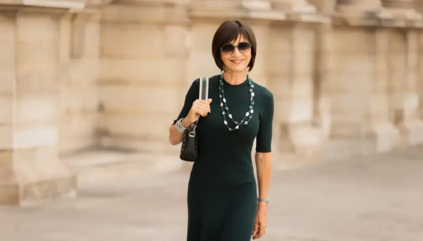 Une femme élégante porte une robe midi vert foncé, un collier de perles et des lunettes de soleil. C'est quoi une robe midi ? C'est une robe qui arrive à mi-mollet.