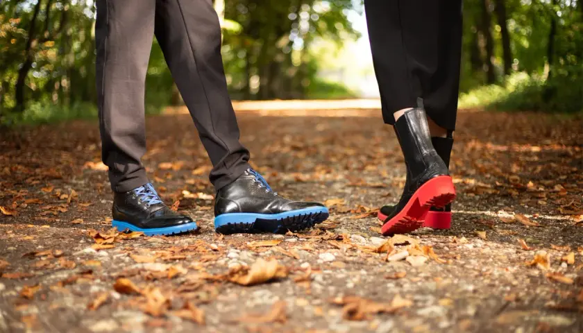 Deux paires de chaussures sur un sentier automnal. L'une a une semelle gomme ou caoutchouc bleue vive, l'autre une semelle rouge éclatante.