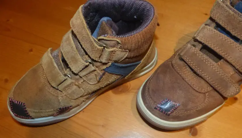 Paire de bottines marron avec des patchs noirs et roses sur le bout de chaussure abîmé.