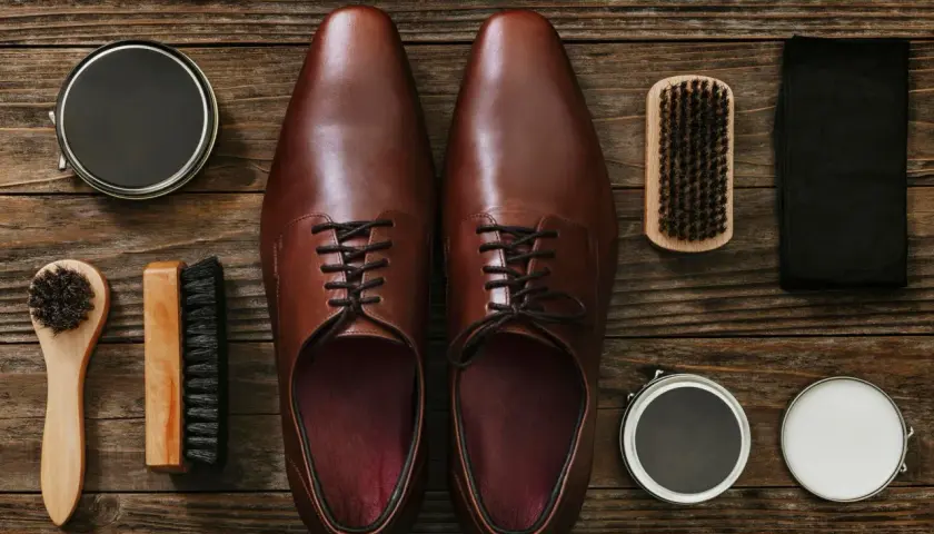 Paire de chaussures en cuir marron, prête pour un entretien. Brosse, cirage et chiffon pour protéger le cuir de la pluie.