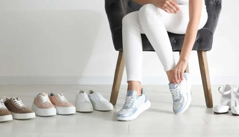 Choix de baskets pour une petite taille : une femme essaie des baskets bleues et blanches, entourée de plusieurs paires de chaussures.