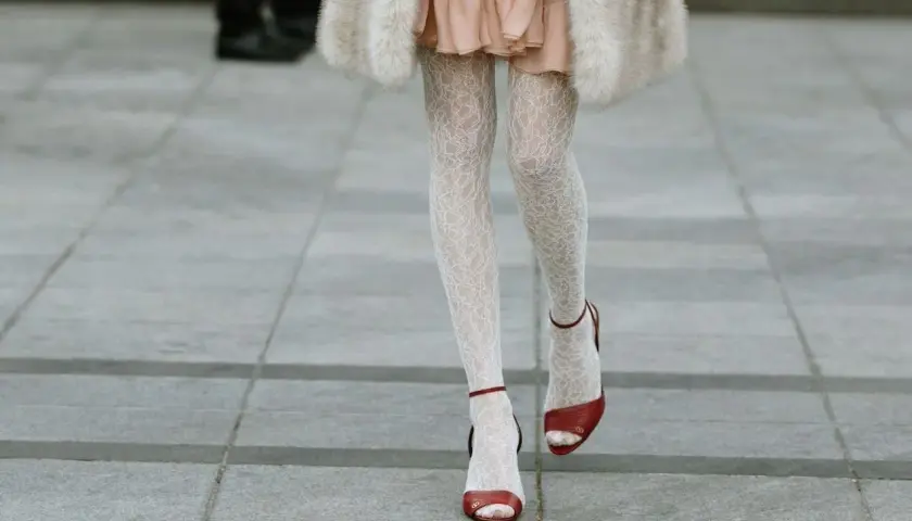 Jambes portant une chaussure ouverte avec collant blanc en dentelle, robe rose et manteau de fourrure.