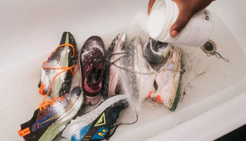 Une main verse une poudre blanche sur plusieurs paires de baskets dans une baignoire. C'est une étape clé pour savoir comment désinfecter des chaussures.