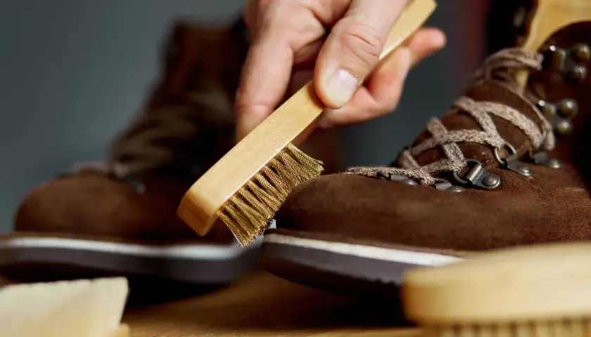 Maintenir vos chaussures en daim beige impeccables : une main utilise une brosse pour nettoyer le daim.