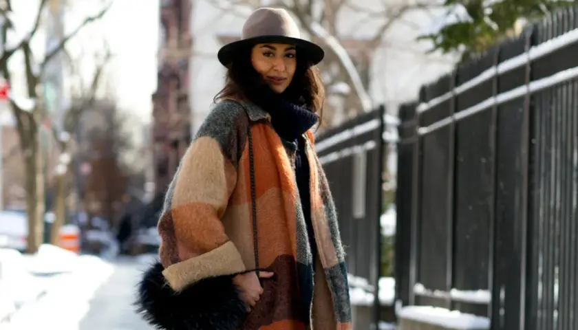 Une femme élégante avec un manteau coloré, un chapeau et un sac en fourrure, parfaite pour savoir comment s'habiller en hiver femme.