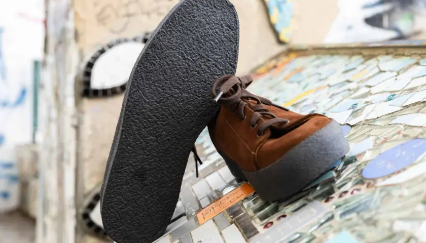 Une semelle crêpe noire repose contre une chaussure marron en daim. Le motif texturé de la semelle crêpe offre une adhérence robuste.