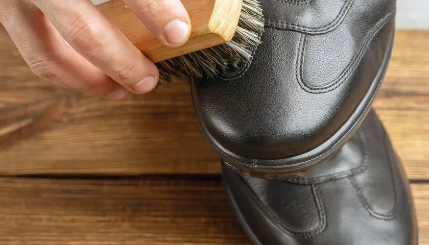 Maintenir le cuir en bon état : une brosse nettoie une chaussure noire pour réparer le cuir craquelé.