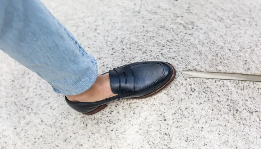 Un pied en jean bleu porte un mocassin bleu marine. La semelle extérieure de la chaussure, signée par un cordonnier, est visible.