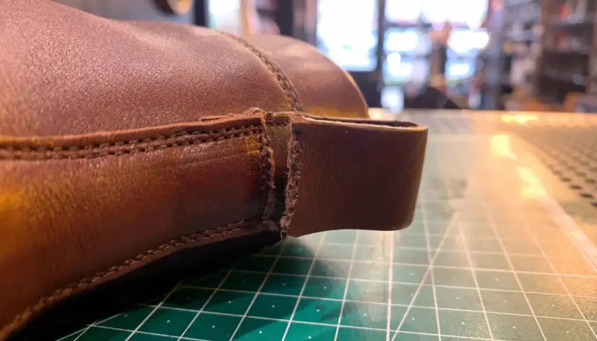 Gros plan sur une chaussure en cuir marron, montrant une déchirure à réparer. Le travail de réparation du cuir déchiré d'une chaussure est en cours.