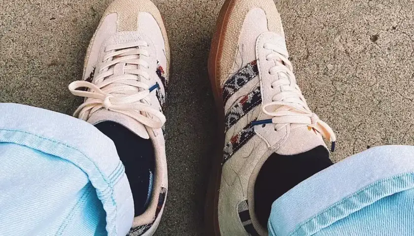 Un homme porte des sneakers Adidas beige avec des détails ethniques, un outfit décontracté parfait pour la belle saison.