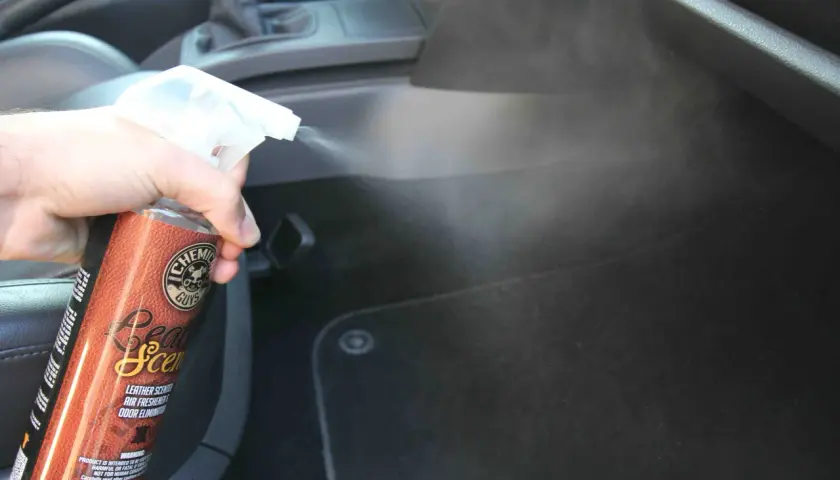 Une main vaporise un produit pour voiture, diffusant une agréable odeur de cuir dans l'habitacle.