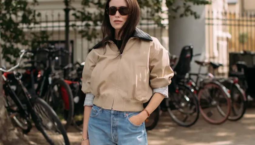 Une femme avec une morphologie H porte un jean bleu délavé et une veste beige.