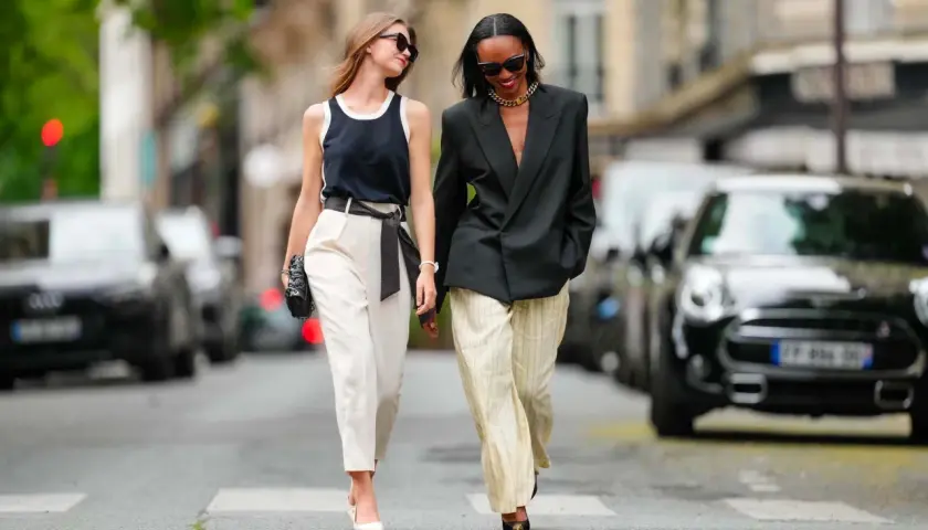 Deux femmes marchent dans la rue. L'une porte un pantalon blanc et un top noir, l'autre un blazer noir et un pantalon rayé. Idées pour comment s'habiller quand on est mince et petite.