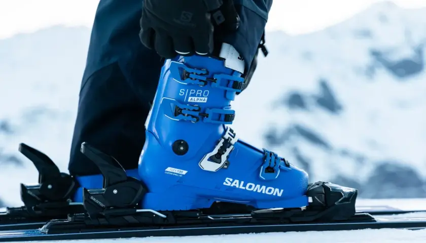 Une chaussure de ski Salomon bleue vif, prête pour la piste. Les boucles noires et blanches sont ajustées, la neige est au rendez-vous.