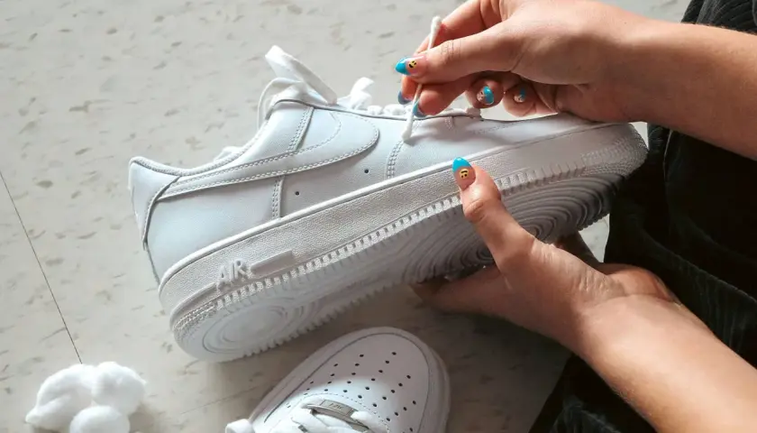 Main blanche, on nettoie une chaussure qui couine avec un coton-tige. Les ongles sont décorés de visages souriants.