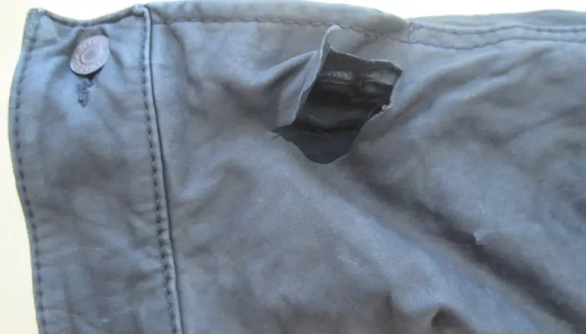 Gros accroc sur un vêtement en cuir, révélant la doublure intérieure. Le bouton sur le côté gauche est intact.