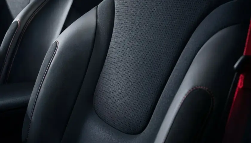 Sièges de voiture en cuir noir et matière alcantara, avec surpiqûres rouges contrastantes.