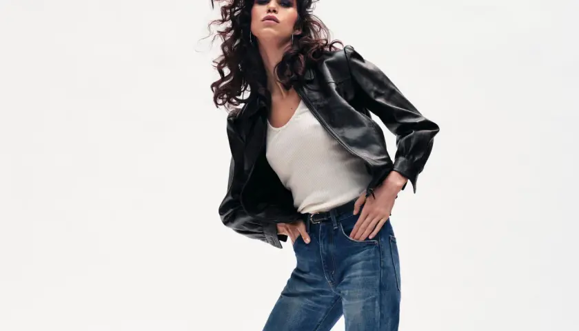 Une femme rock'n'roll pose avec un jean droit, une veste en cuir et un top blanc. Un look intemporel pour savoir comment porter un jean droit femme avec style.