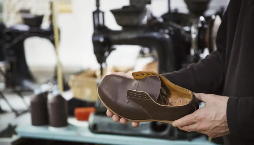 Un artisan examine une chaussure de ville en cuir marron, signe qu'il est temps de penser à quand changer ses chaussures de ville.
