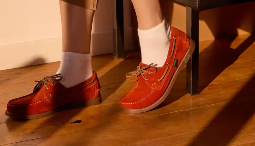 Chaussure bateau femme look : des mocassins en daim orange vif avec lacets en cuir, portés avec des chaussettes blanches sur un parquet en bois.