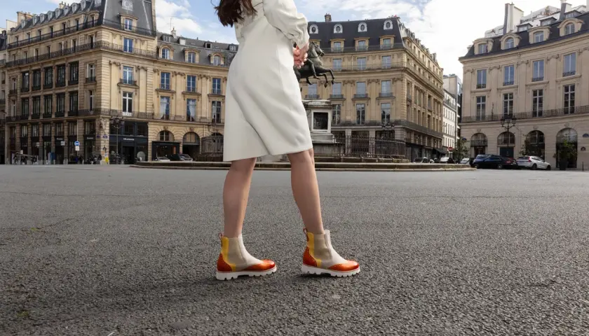 Une femme porte des bottines colorées en plein été, marchant sur une place parisienne.