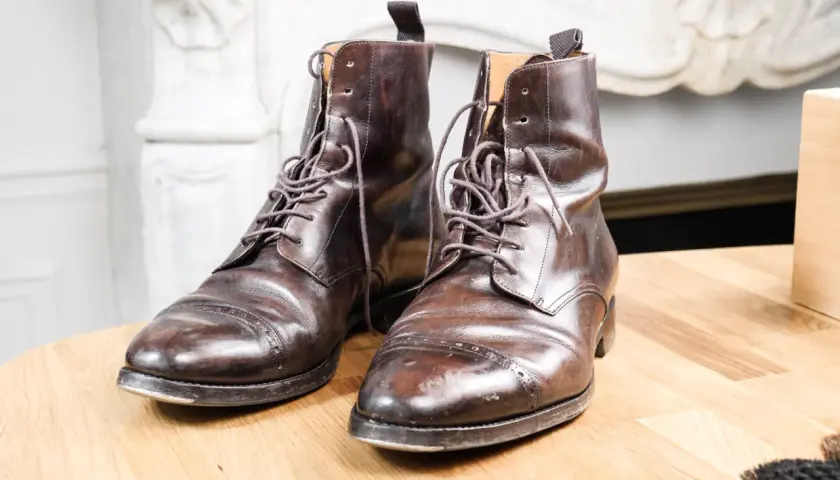 Paire de bottines en cuir griffé marron foncé, lacets serrés, posées sur une table en bois.
