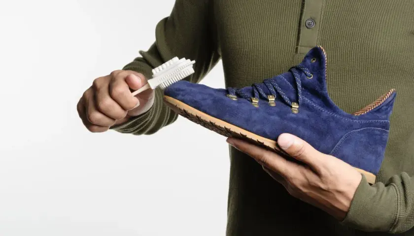 Maintenir le cuir suédé en bon état : une main brosse une chaussure bleue avec une brosse spéciale.