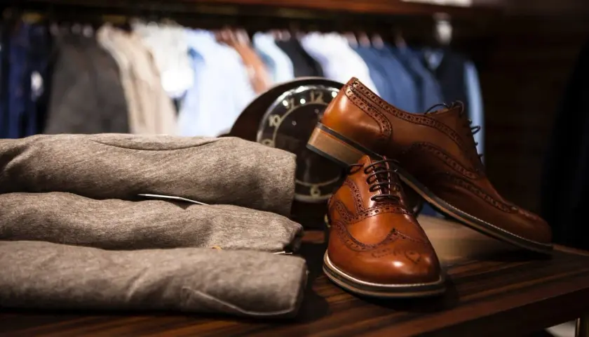 Chaussures en cuir marron élégantes, prêtes à être assouplies. Un pull plié et un manteau sont visibles en arrière-plan.