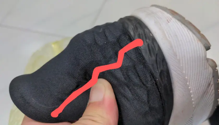 Un pouce appuie sur le contrefort d'une chaussure noire, révélant une fissure.