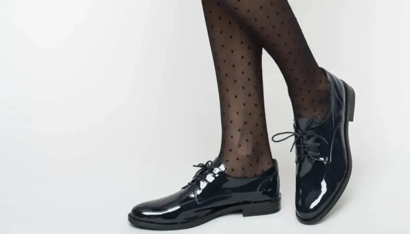 Pieds chaussés de derbies vernies et collants à pois. Idéal pour savoir comment porter des derbies femme avec élégance.
