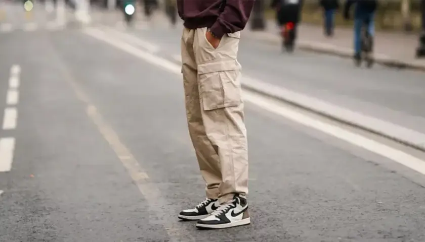 Un homme porte un pantalon cargo beige et une chaussure de sport iconique, prêt pour une journée en ville.