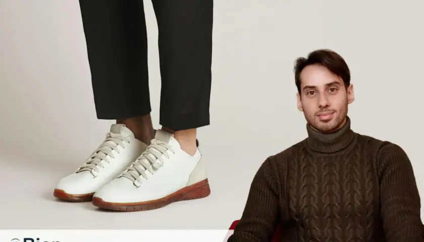 Un homme porte un pull à col roulé et un pantalon cigarette avec une chaussure blanche.
