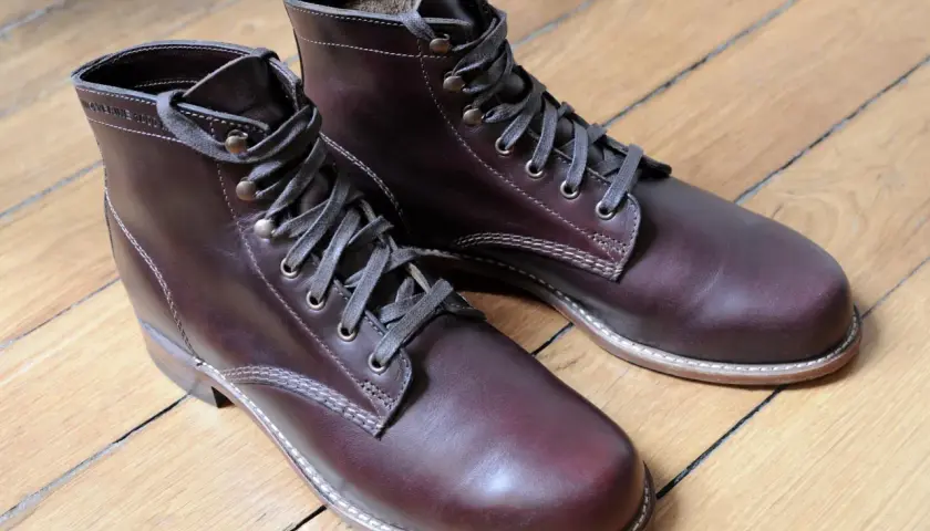 Bottes marron en cuir gras, lacets gris, sur un parquet en bois.