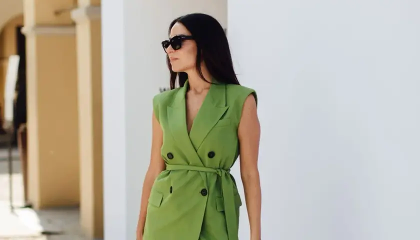 Une femme en robe blazer verte, lunettes de soleil, incarne pourquoi bien s'habiller au travail : confiance et professionnalisme.