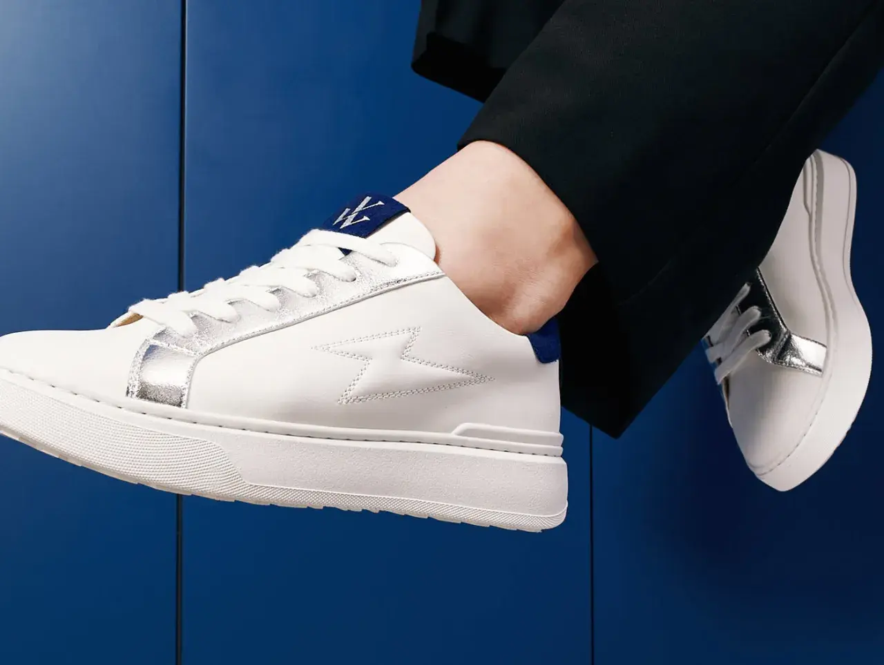 Baskets blanches homme avec détails argentés et logo bleu. Parfaites avec un pantalon noir, elles répondent à la question : quelles chaussettes avec baskets blanches homme ?