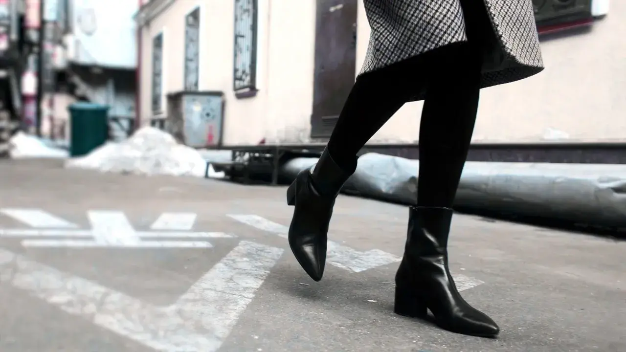 Une femme porte une tenue élégante avec des chelsea boots femme noires, un manteau à carreaux et des collants.
