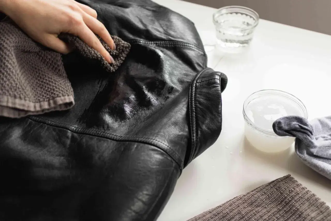 Maintenant, découvrez comment nettoyer une veste en simili cuir. Une main utilise un chiffon pour frotter la veste noire.