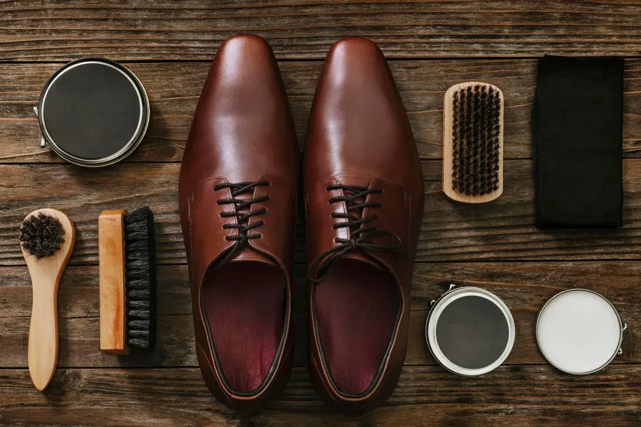 Paire de chaussures en cuir marron, prête pour un entretien. Brosse, cirage et chiffon pour protéger le cuir de la pluie.
