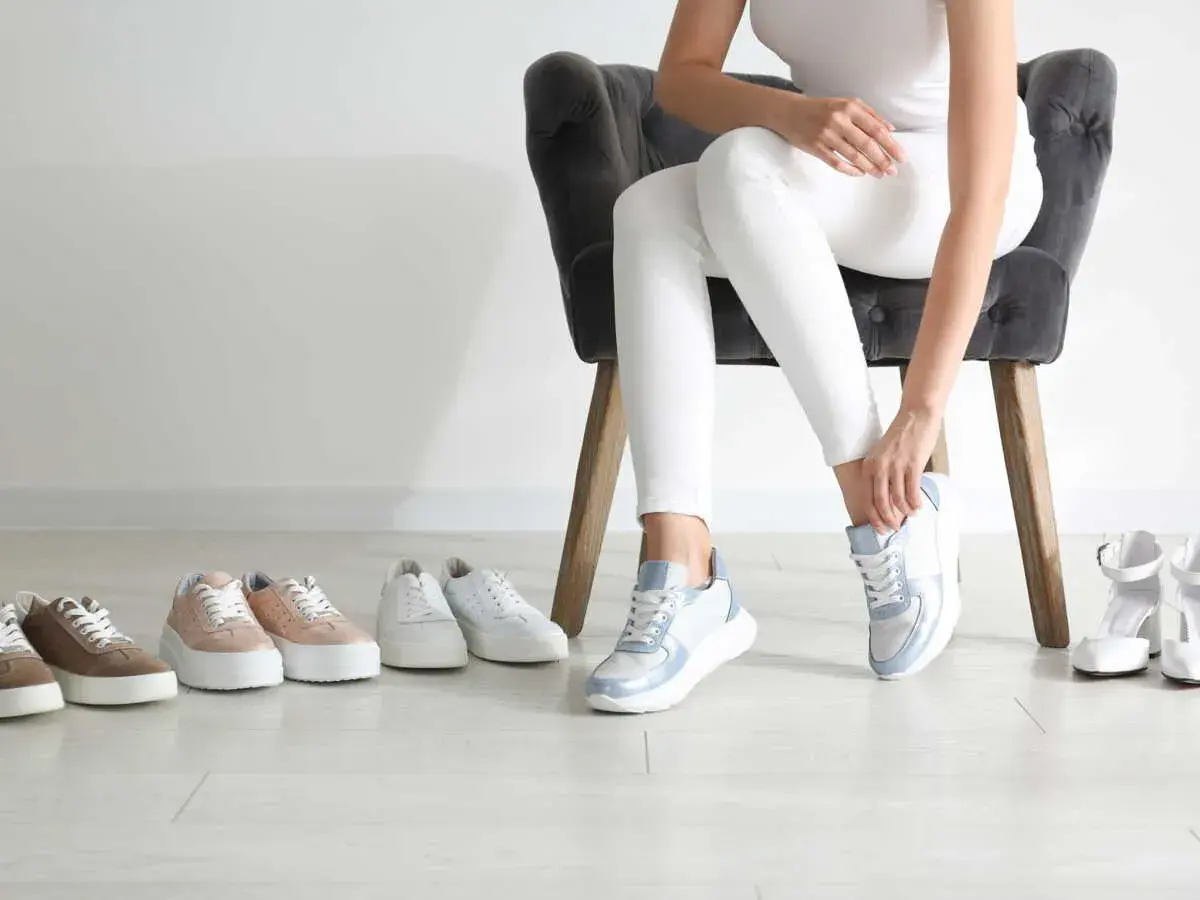 Choix de baskets pour une petite taille : une femme essaie des baskets bleues et blanches, entourée de plusieurs paires de chaussures.