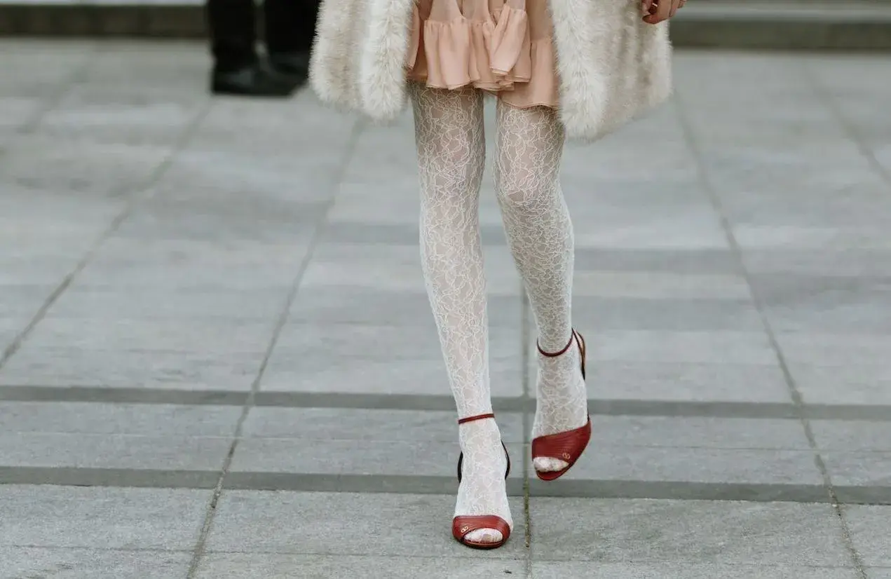 Jambes portant une chaussure ouverte avec collant blanc en dentelle, robe rose et manteau de fourrure.