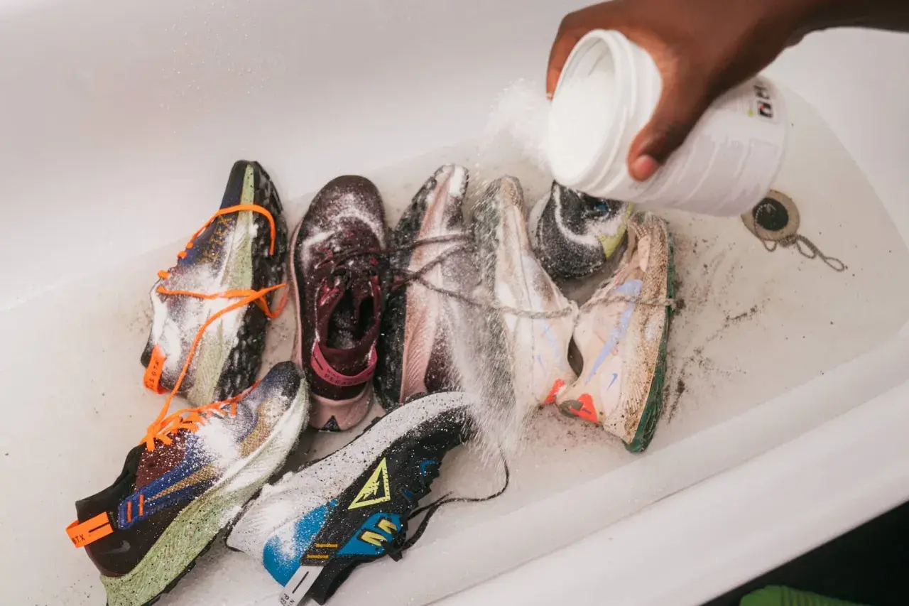 Une main verse une poudre blanche sur plusieurs paires de baskets dans une baignoire. C'est une étape clé pour savoir comment désinfecter des chaussures.