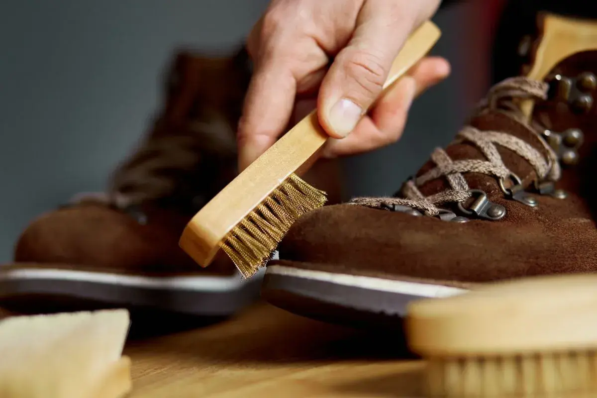 Maintenir vos chaussures en daim beige impeccables : une main utilise une brosse pour nettoyer le daim.