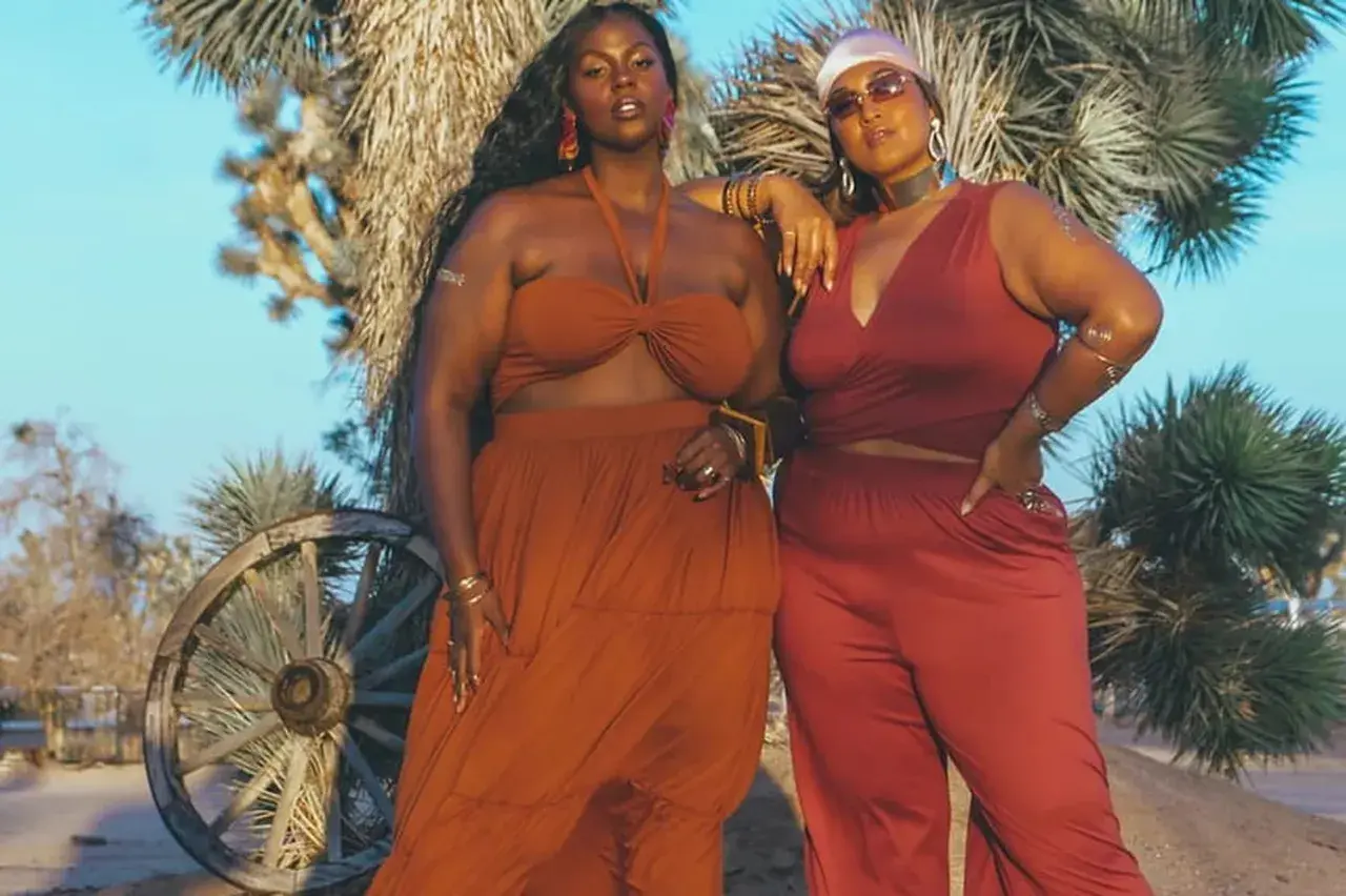 Deux femmes aux courbes généreuses posent dans le désert. L'une porte une robe longue orange, l'autre un ensemble pantalon et top rouge. Des tenues parfaites pour savoir comment s'habiller quand on a des grosses cuisses.