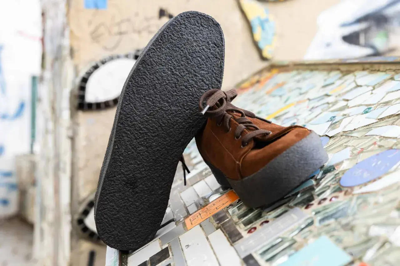 Une semelle crêpe noire repose contre une chaussure marron en daim. Le motif texturé de la semelle crêpe offre une adhérence robuste.