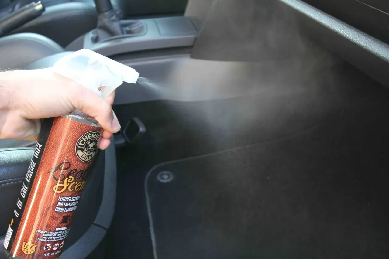 Une main vaporise un produit pour voiture, diffusant une agréable odeur de cuir dans l'habitacle.