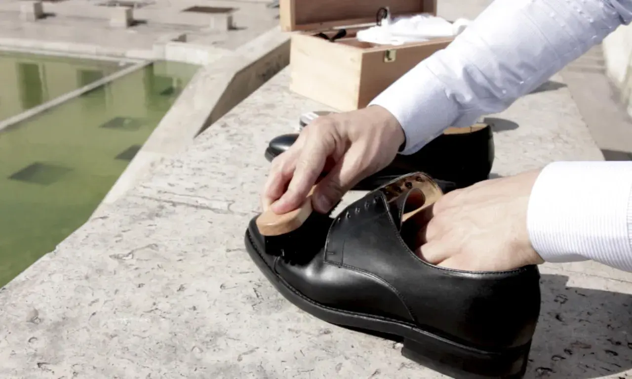 Un homme utilise une brosse pour faire briller ses chaussures en cuir noir, prêt pour une journée élégante.