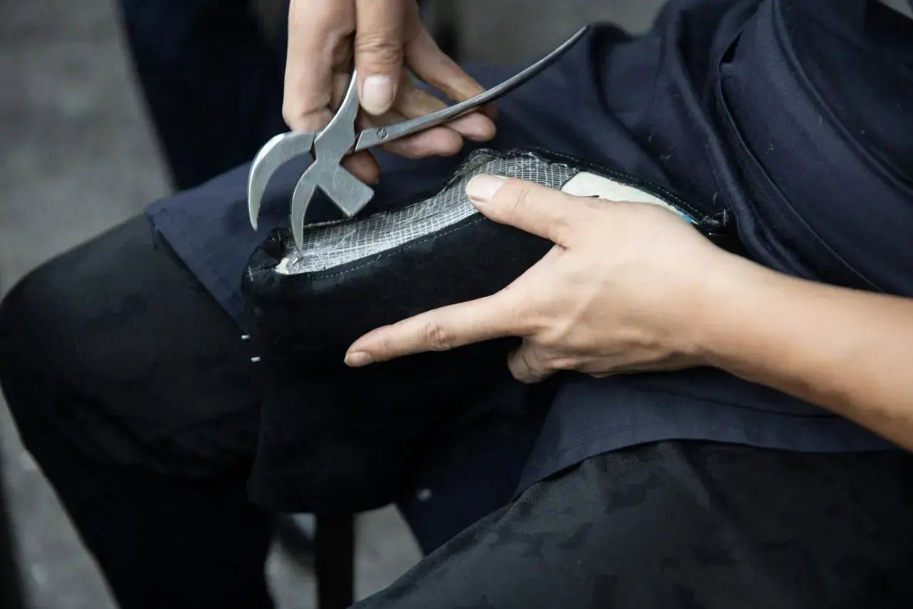 Mains expertes utilisant un outil pour réparer le simili cuir qui s'effrite sur un objet noir.