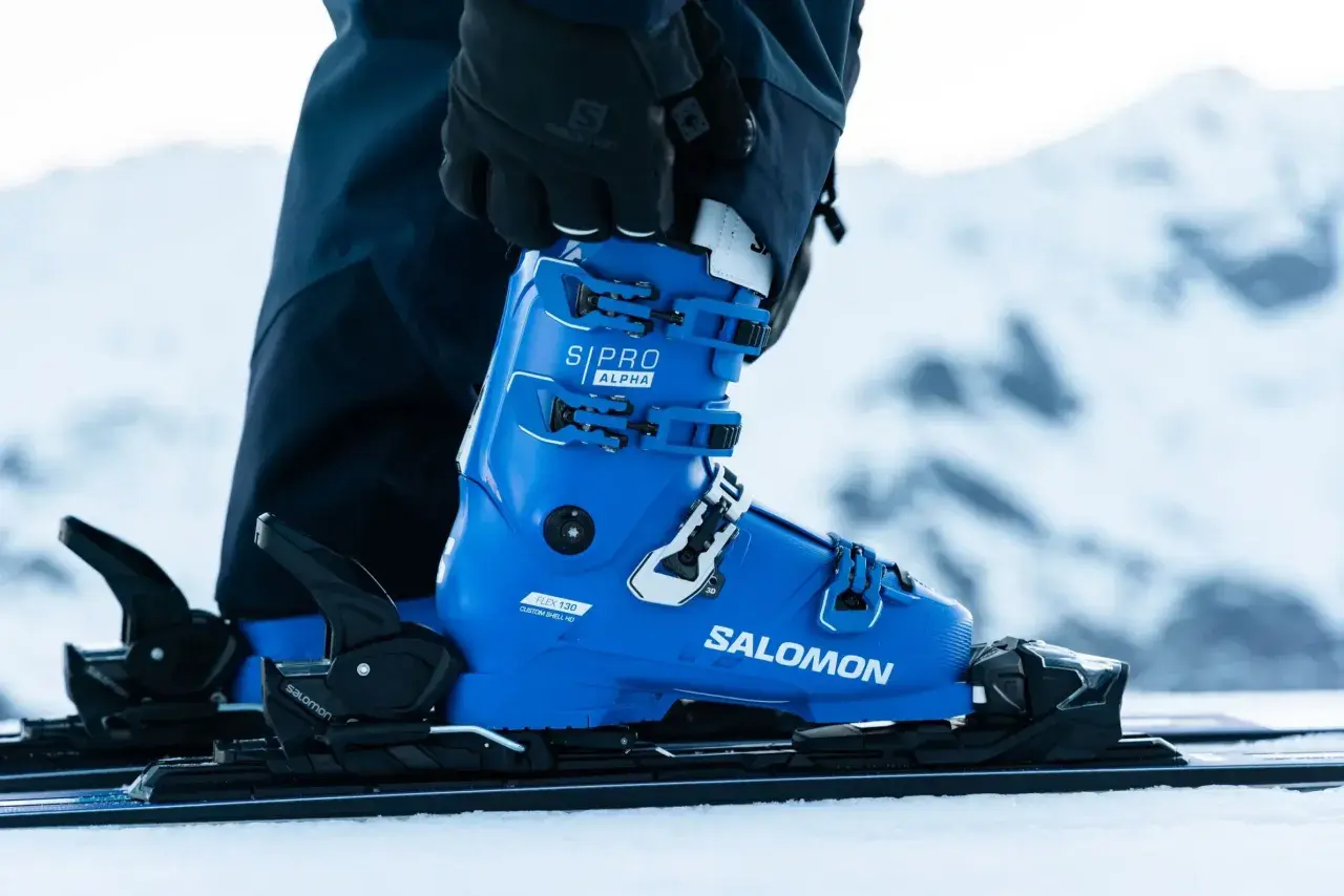 Une chaussure de ski Salomon bleue vif, prête pour la piste. Les boucles noires et blanches sont ajustées, la neige est au rendez-vous.