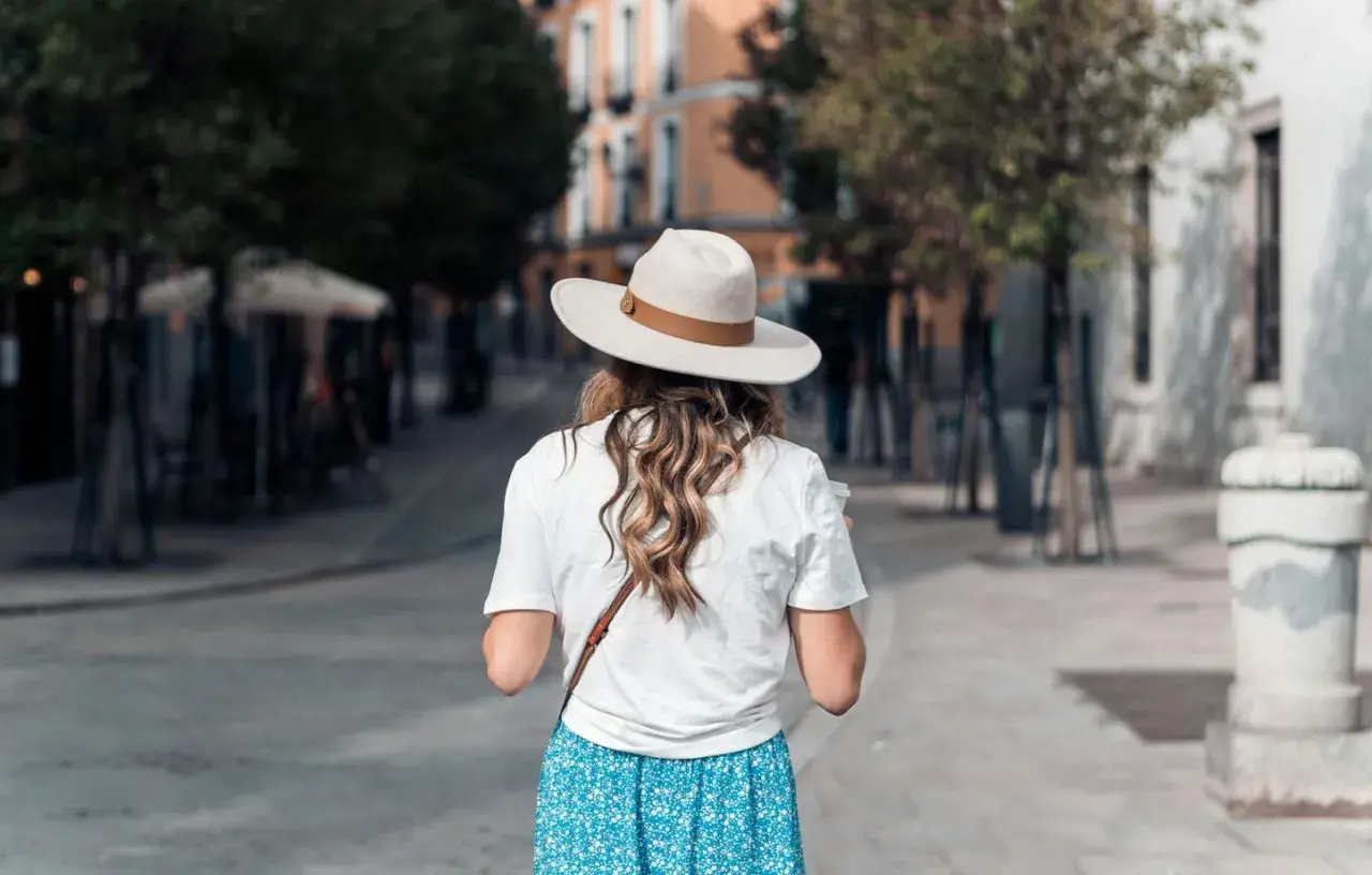 Une femme porte un chapeau et une robe fleurie, idéale pour savoir quelle couleur porter quand il fait chaud.