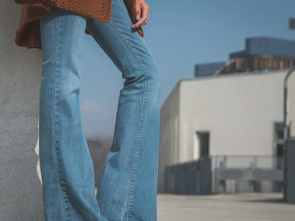 Un jean bootcut bleu clair, un pull marron et des baskets. Style décontracté pour une journée ensoleillée.